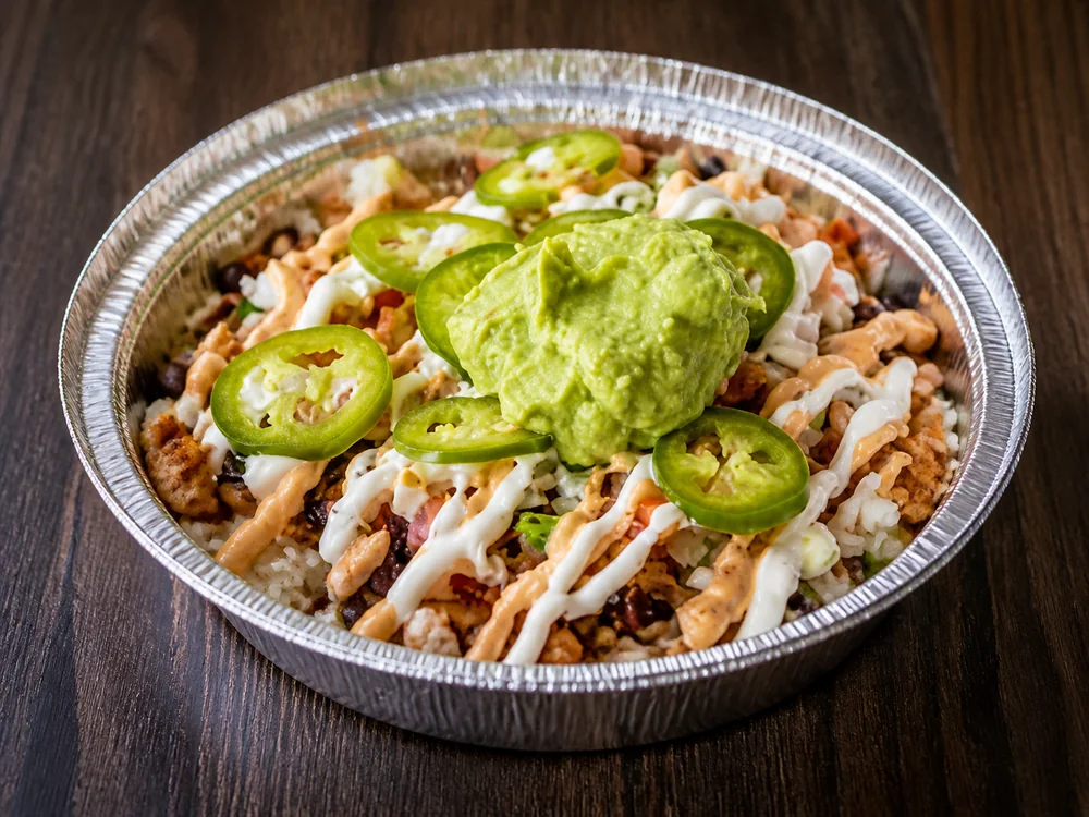 A customizable CocoRay's bowl with rice, beans, protein, sauces, jalapeños, and guacamole